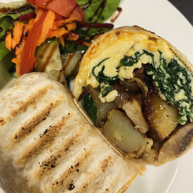Grilled breakfast burrito cut open, filled with omelette, spinach, mushrooms and potatoes