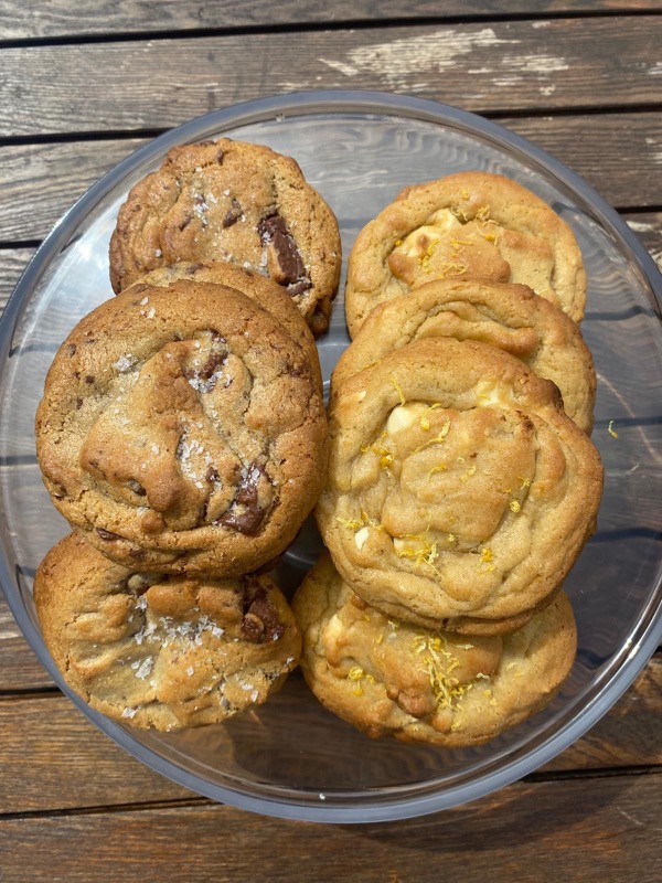 Sea-salted chocolate chunk and lemon white-chocolate cookies piled on a glass cake stand