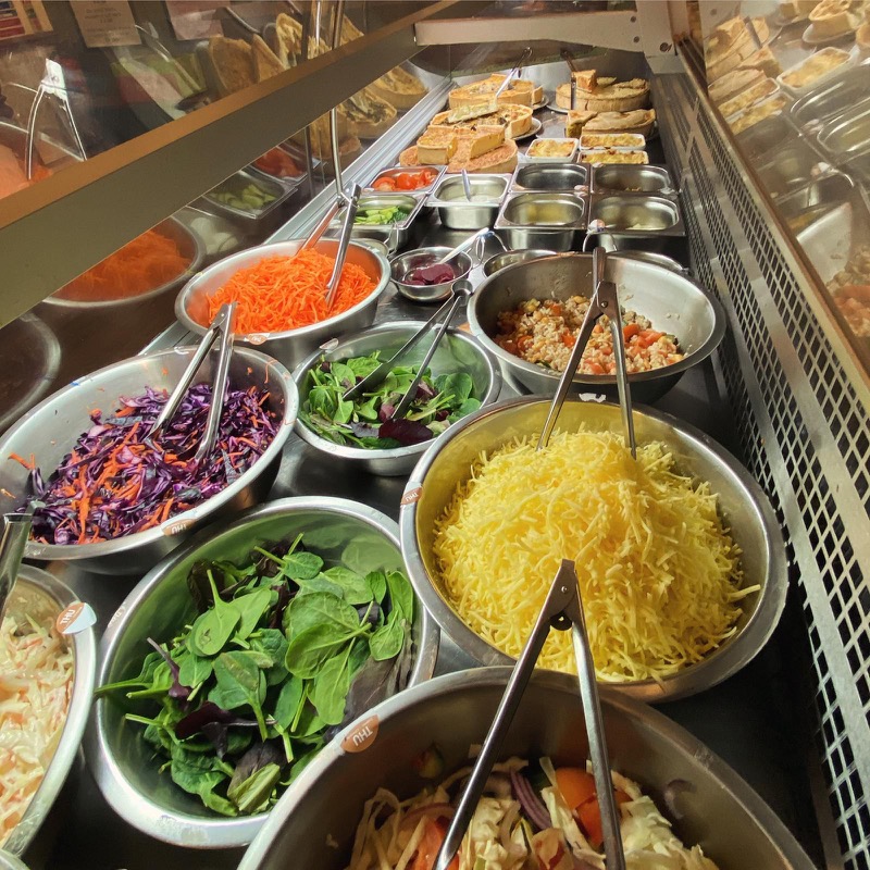 The Crumbs salad bar: bowls of carrot, red cabbage, leaves and cheese with quiches behind the glass